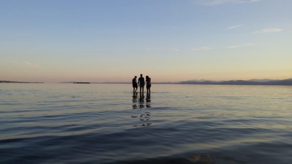 silhouettes standing in the water against a sunset