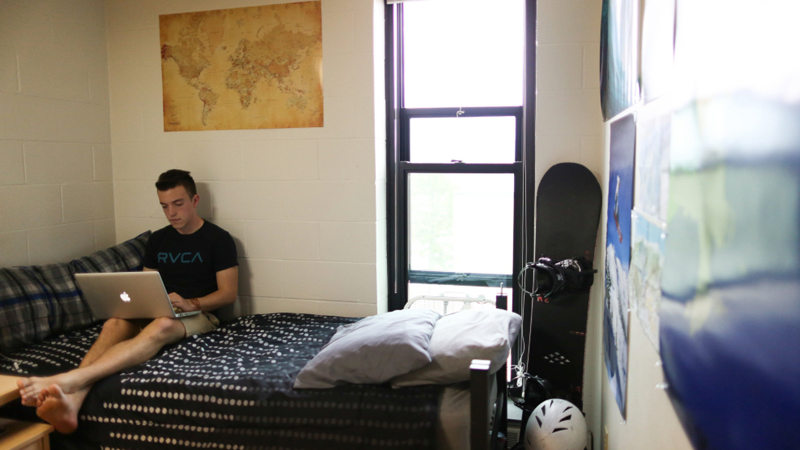 student on a bed in a residence hall room