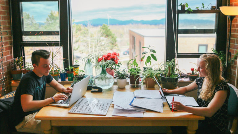 two students in a residence hall room studying at a table in front of a window