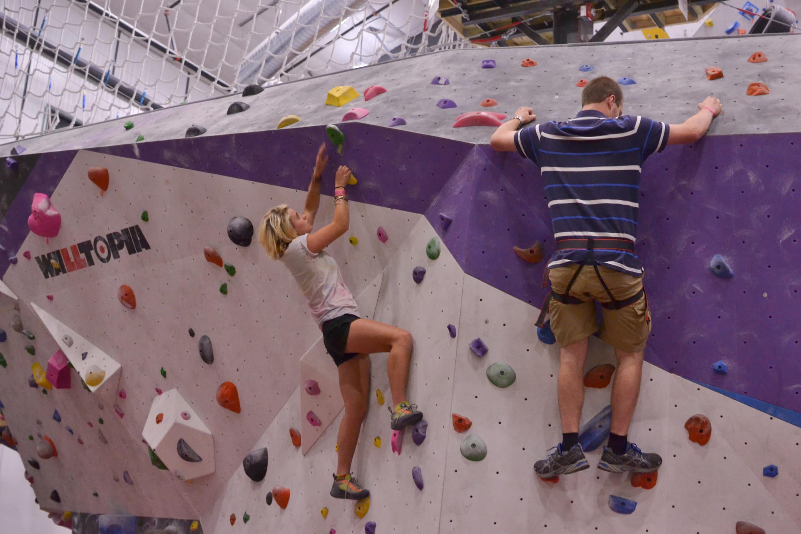 two students climbing along a multi-colored wall