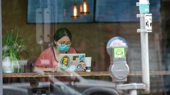 a student sitting in a window at a laptop drinking coffee