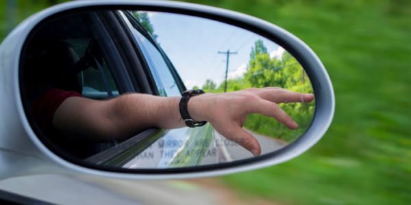 a hand reflected in a review mirror hanging outside a car window