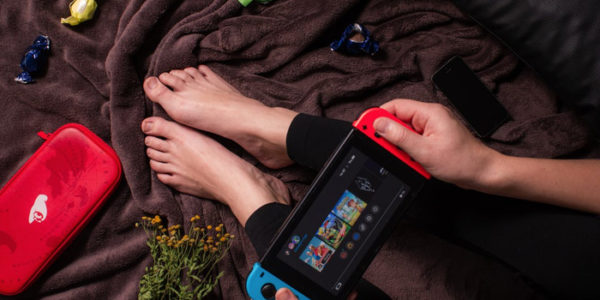 hands holding a nintendo switch on a bed