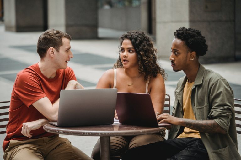three students sitting around a table on their laptops