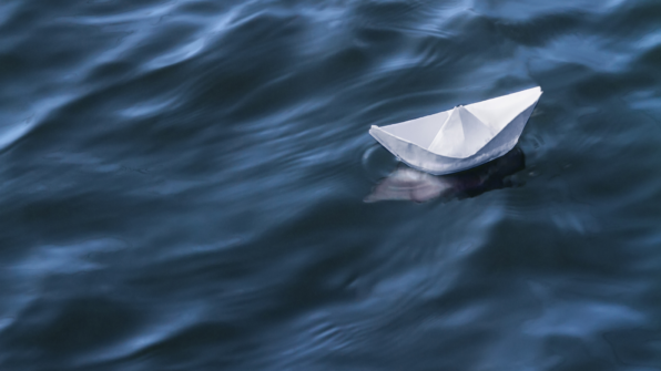A folded paper boat floats in a body of water.