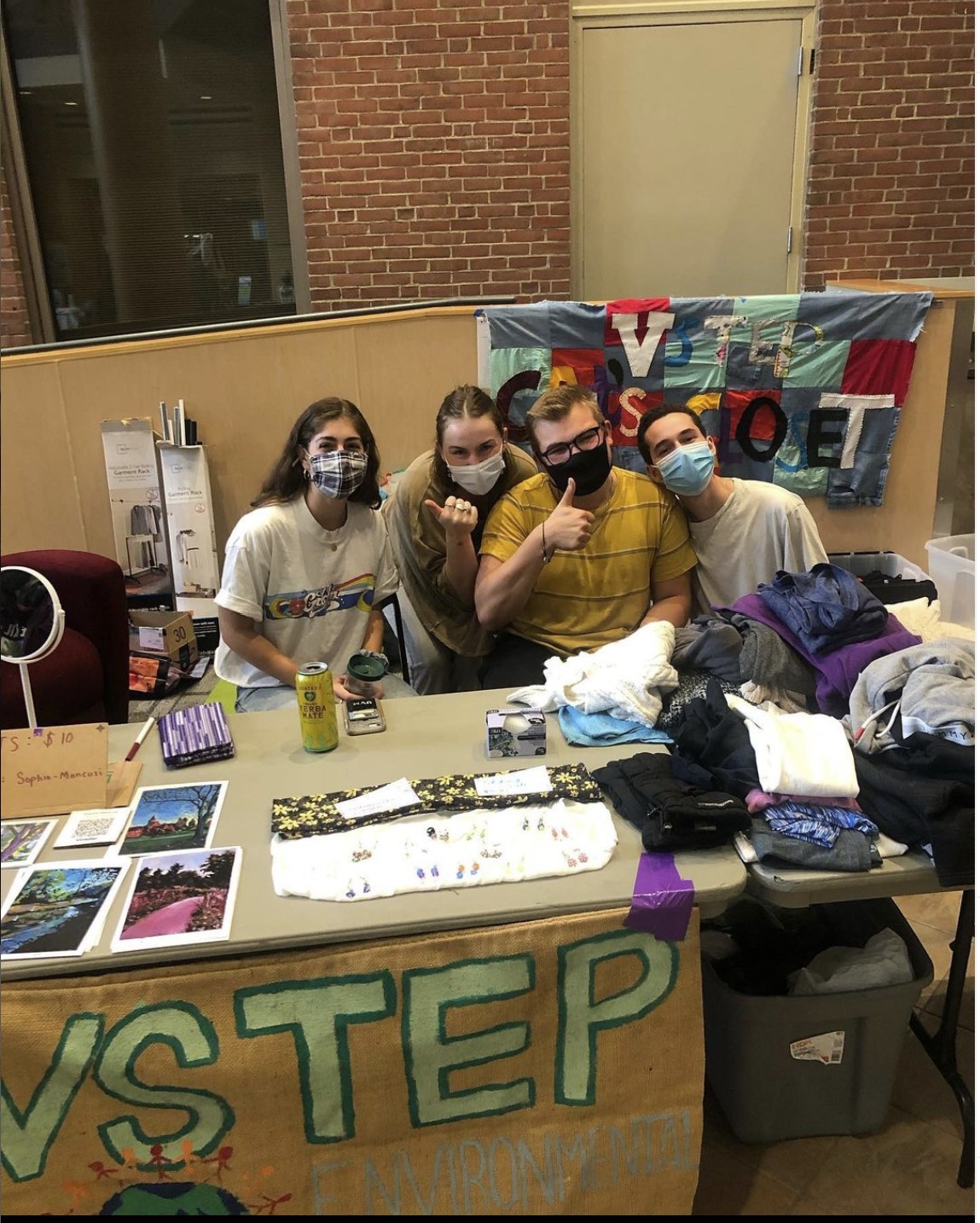 Students sitting behind a table with piles of clothes and a "VSTEP" banner on it.