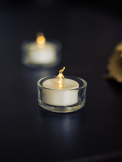 a lit electric tea light sits on top of a black surface