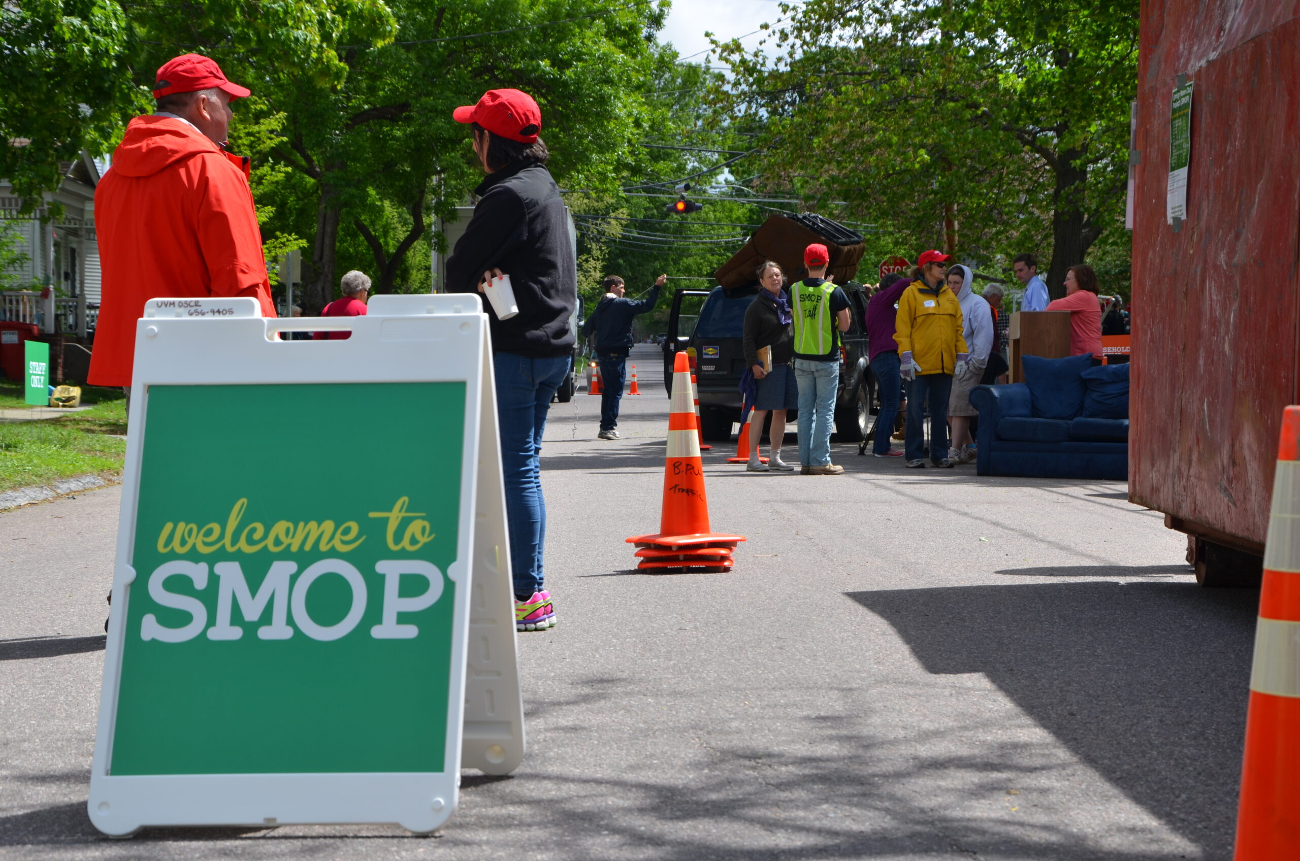A group of people move a couch into a donation truck, and a sign reads "Welcome to SMOP"