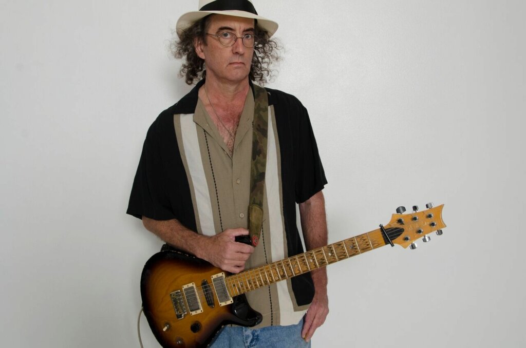 James McMurtry holding an electric guitar against a white background