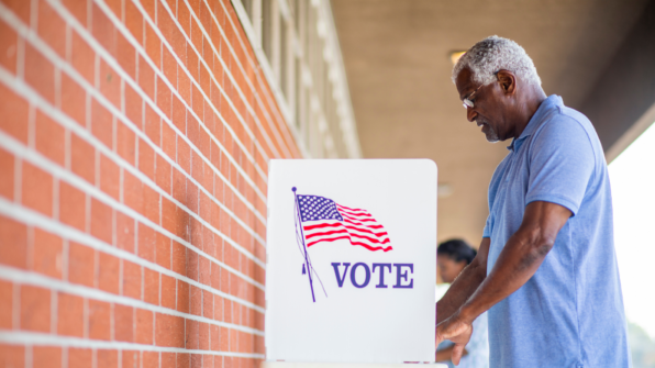 a man standing alone at a voting poll near a large brick wall