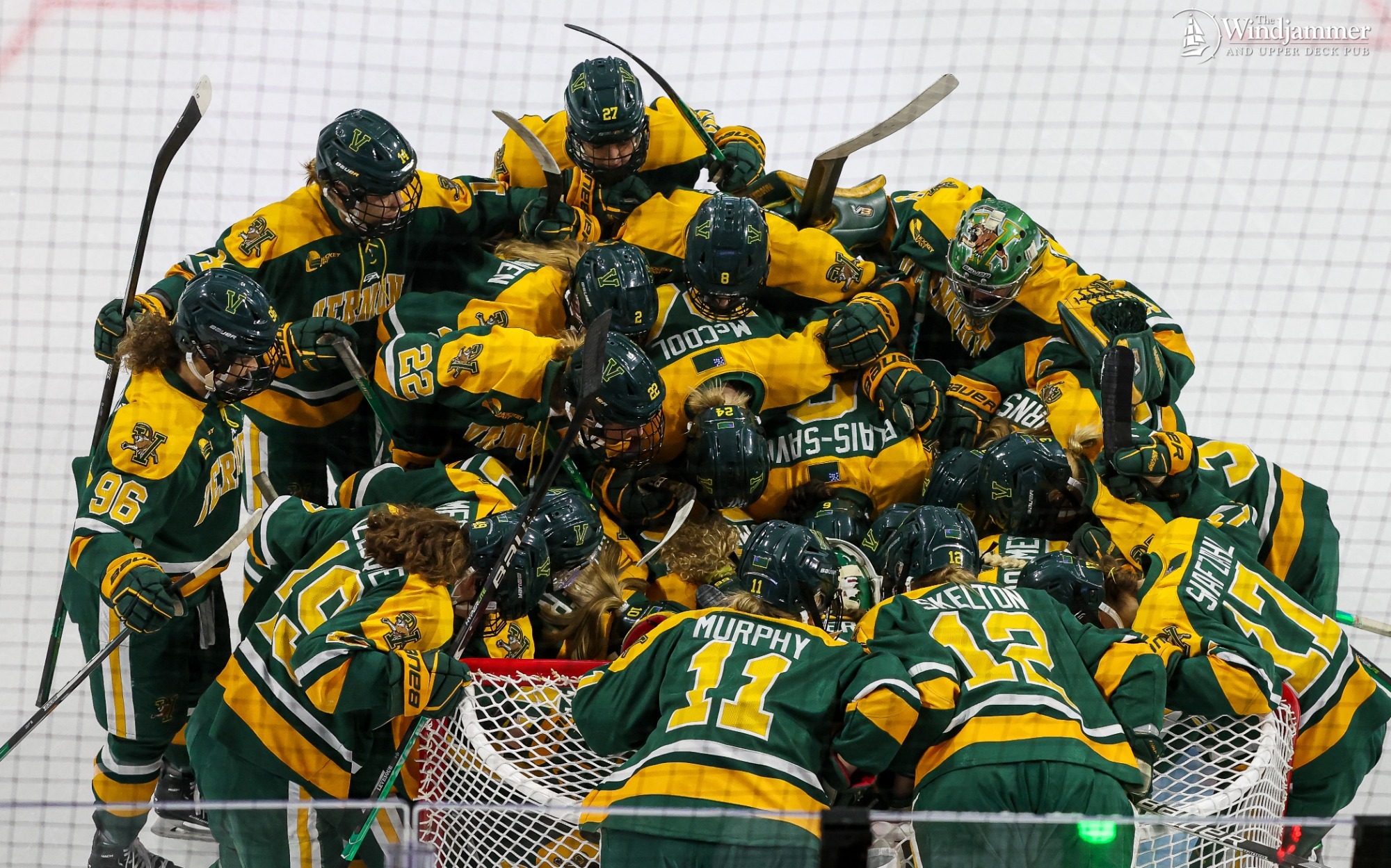 the womens ice hockey team huddle around a goal on the rink