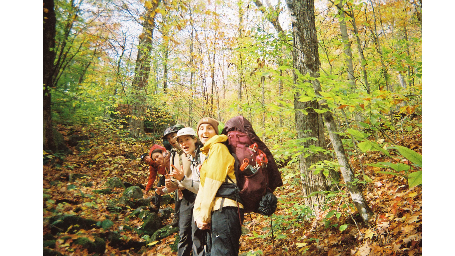 a group of three people in the middle of the frame, with the first one wearing a yellow raincoat and a hiking backpack