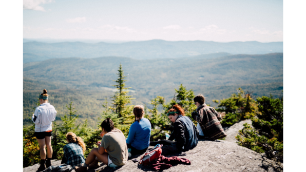 group of young adults sitting on a large rock formation at the top of a mountain