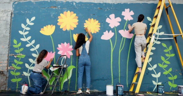 A group of students painting a mural on a wall of brightly colored flowers.