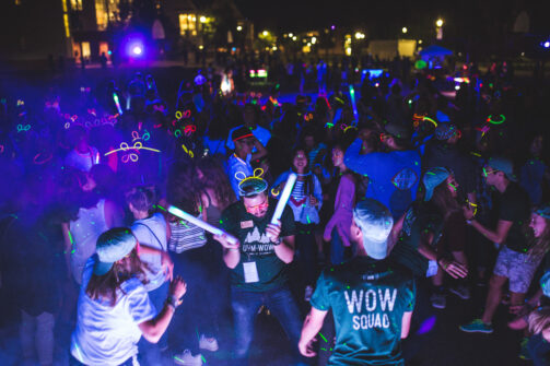 A crowd of UVM students dance at a Week of Welcome event while wearing glow sticks.